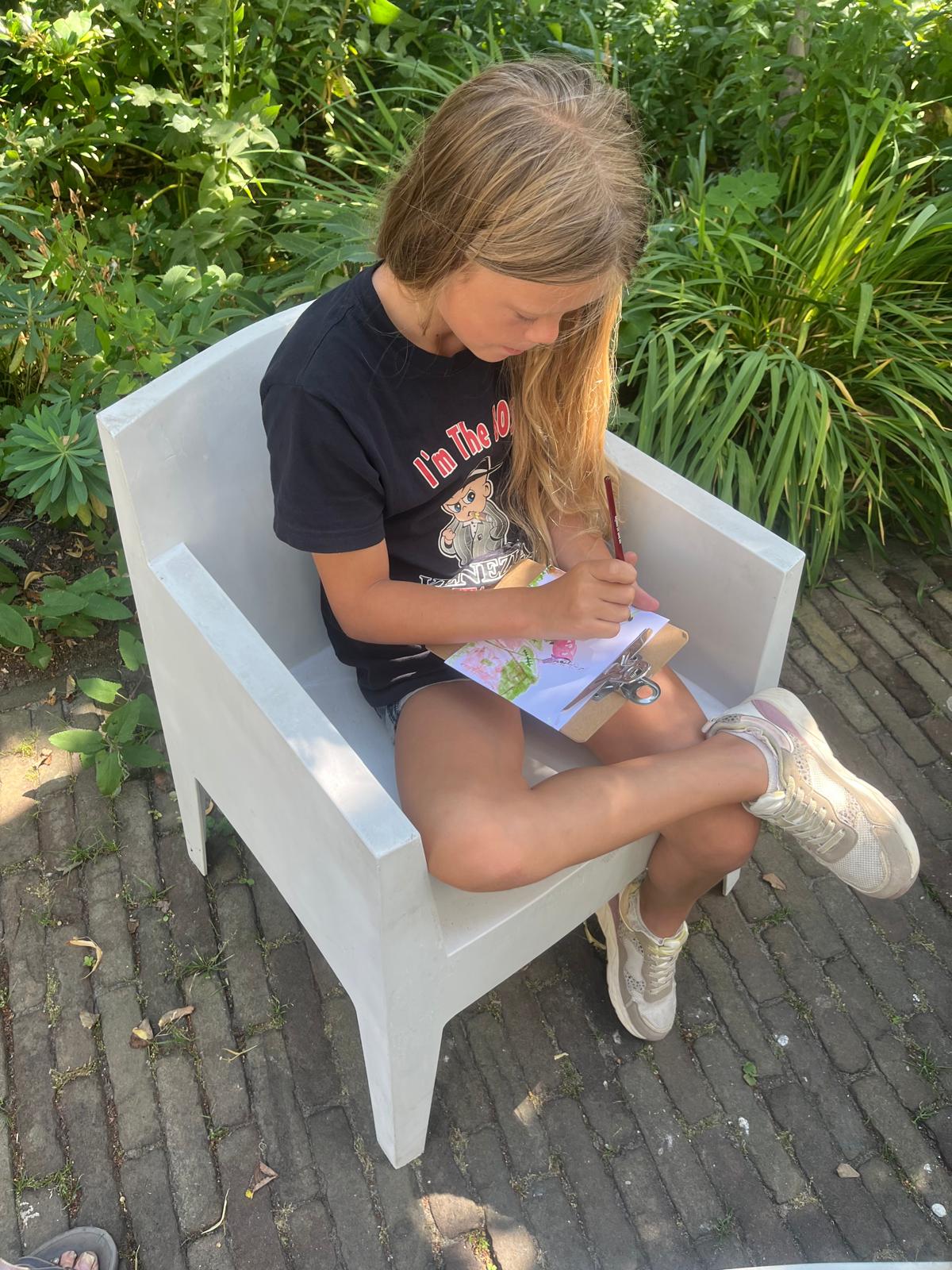 Kind tekent geconcentreerd op een witte tuinstoel