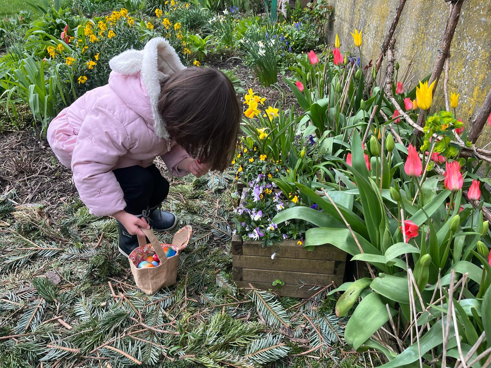 Kind met konijnenoren zoekt paaseieren tussen de tulpen