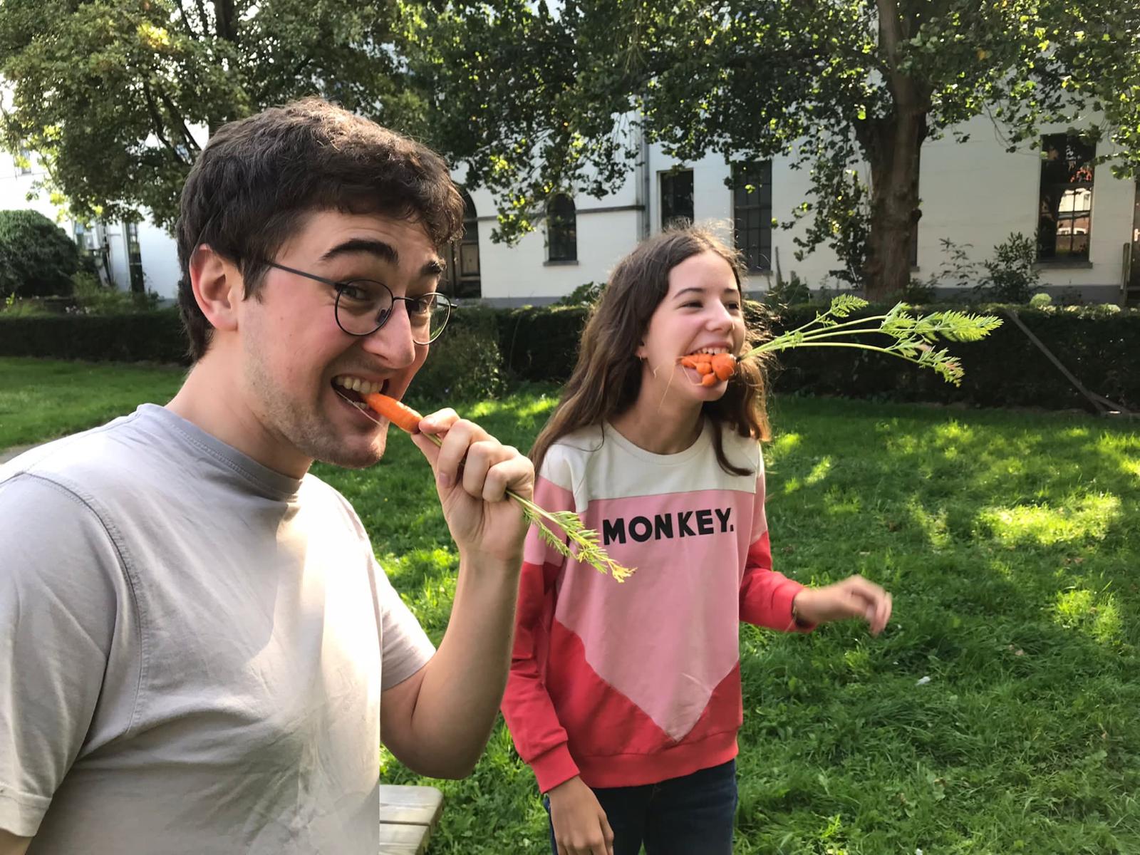 Twee jongeren eten net geoogste wortels uit de tuin