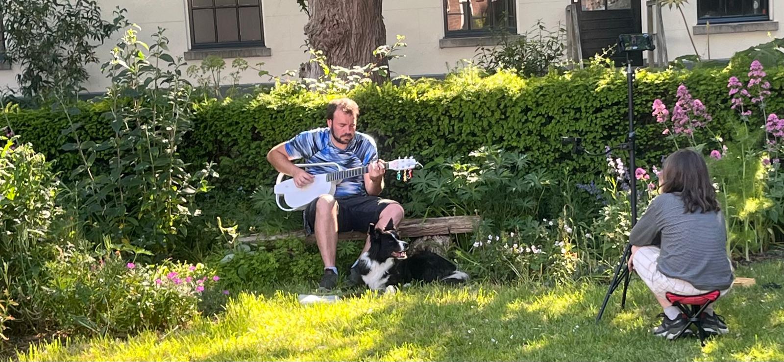 Muzikant speelt mandoline op een bankje in de tuin met hond ernaast