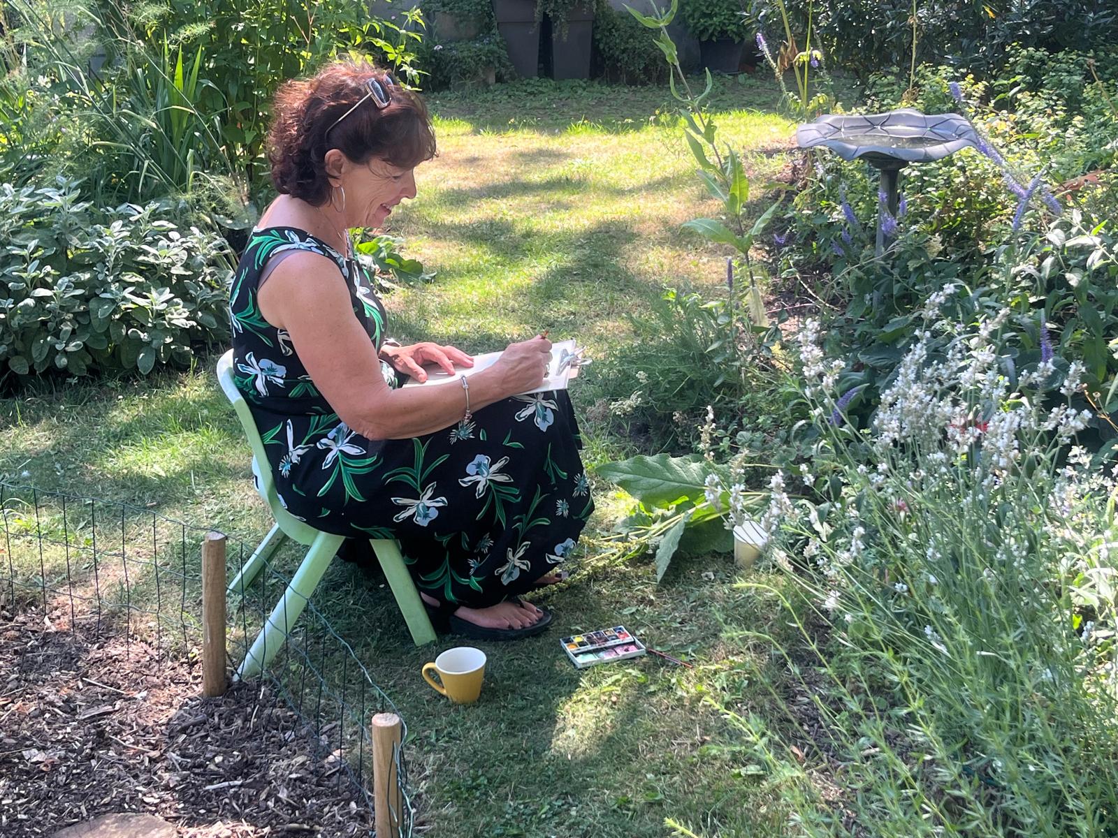 Vrouw schetst geconcentreerd in de tuin bij het vogelbad