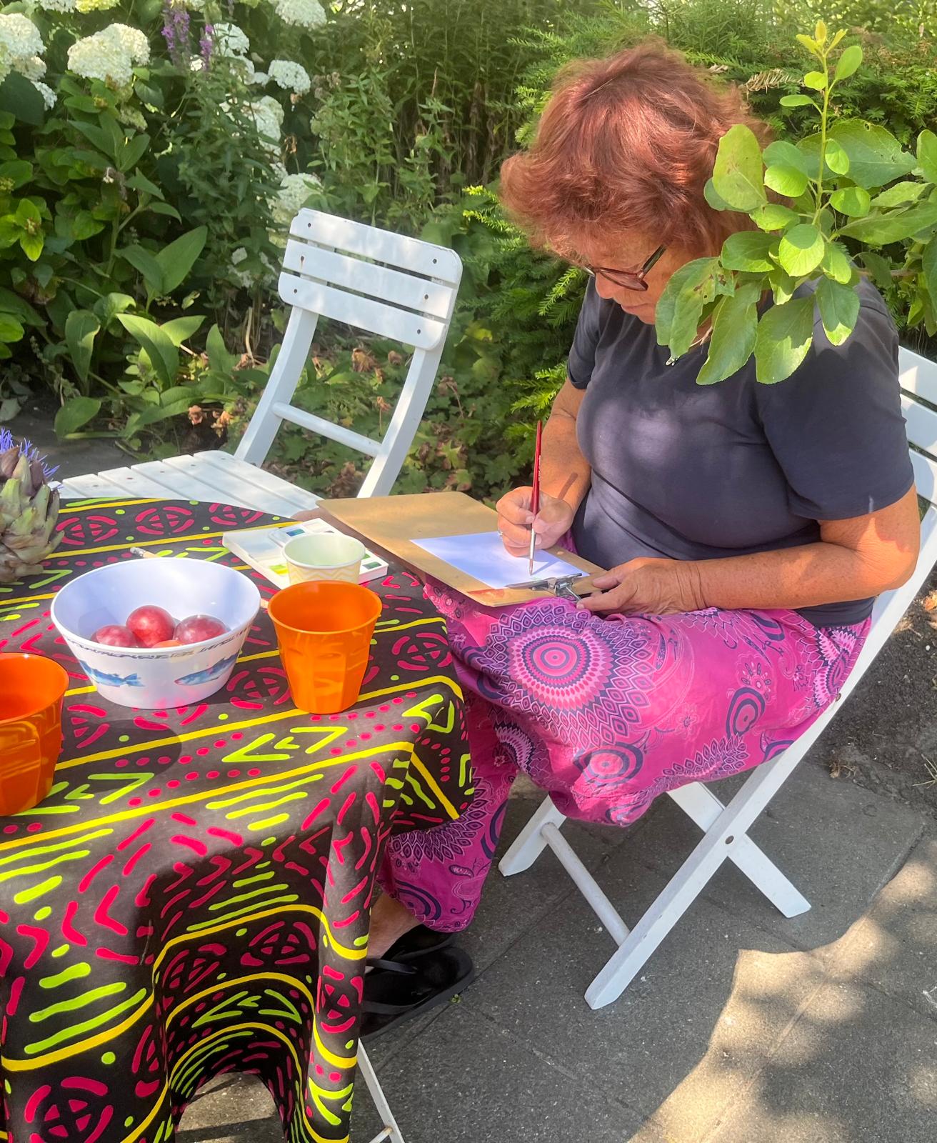 Vrouw schildert met aquarelverf aan een tuintafel